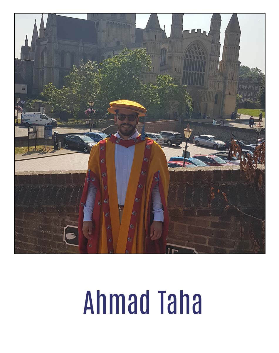 Alumnx AHmad Taha standing in graduation robes outside Rochester Cathedral, smiling at camera